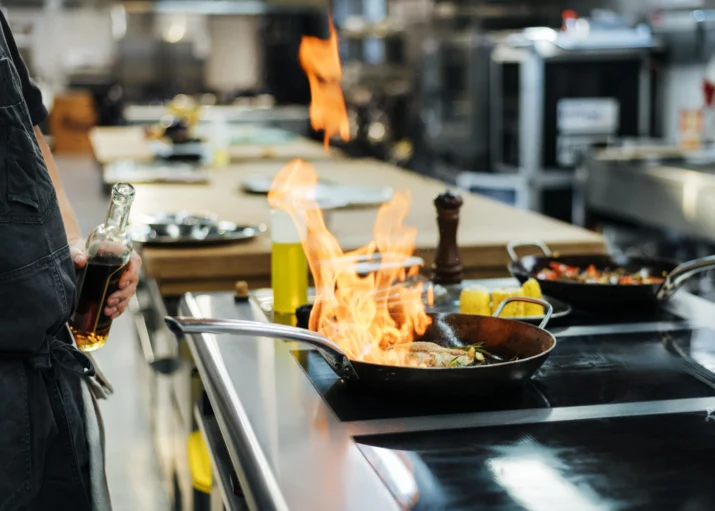 vue laterale du chef flambant un plat dans la cuisine